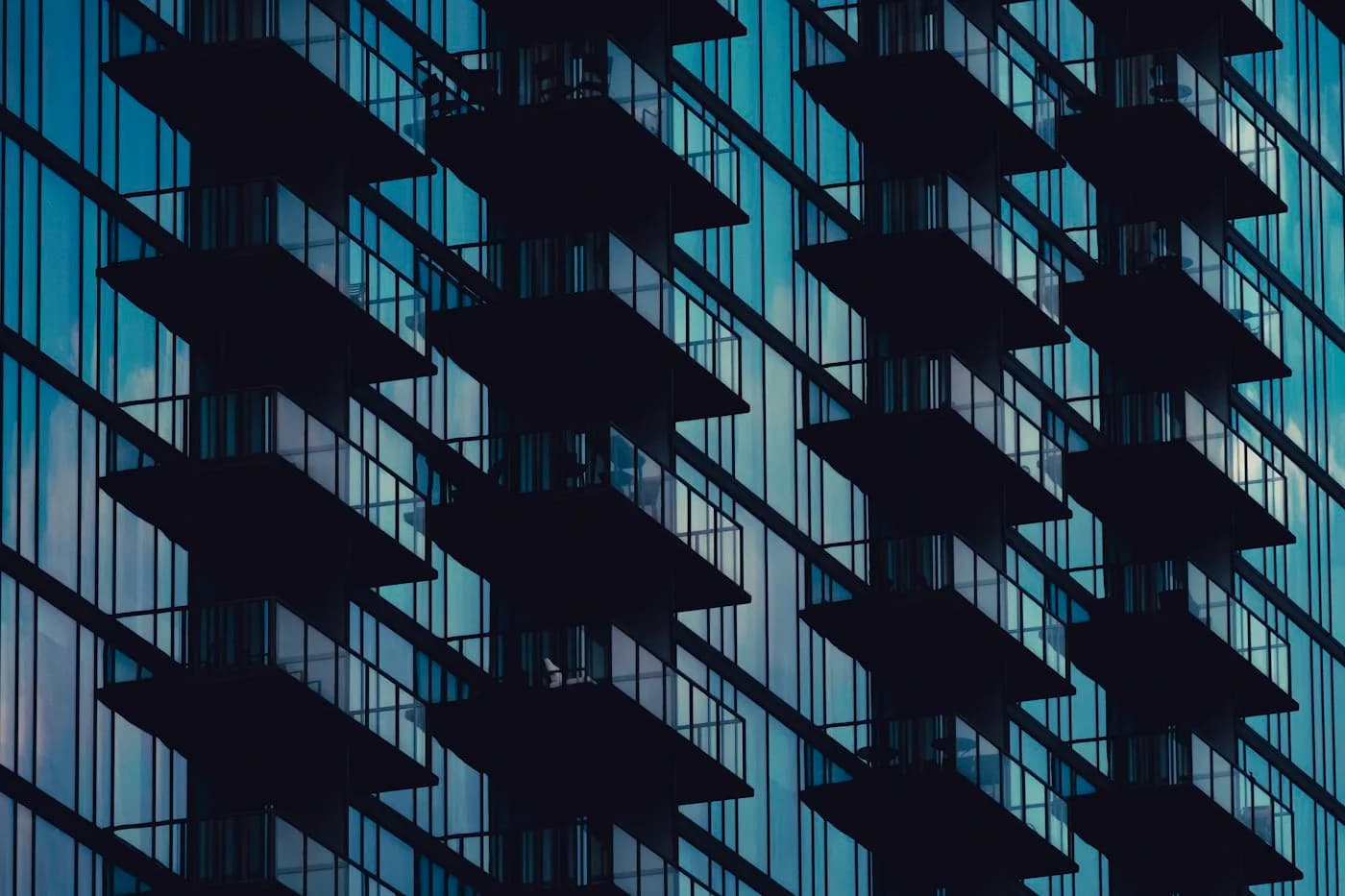 Glass high-rise facade with projecting balconies and reflected blue sky